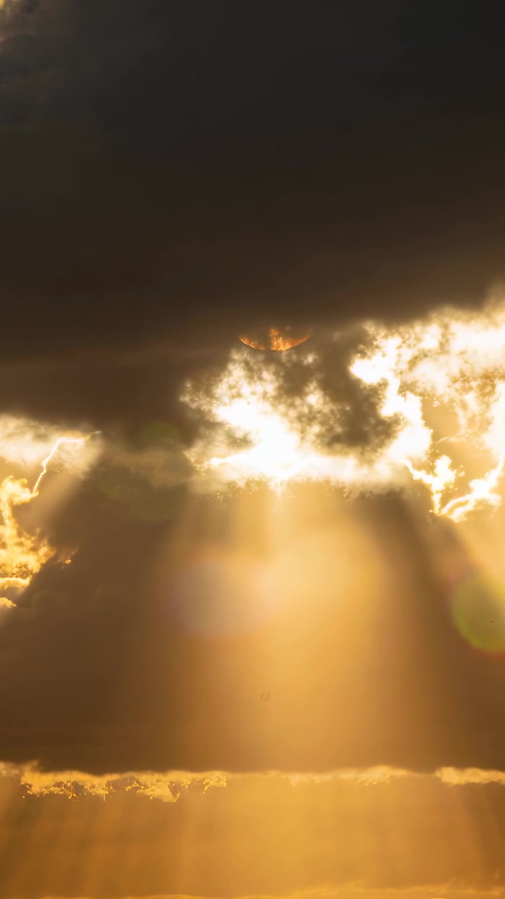 Vertical video: Sun casting beams via gap at horizon with shifting clouds making flicker and flare