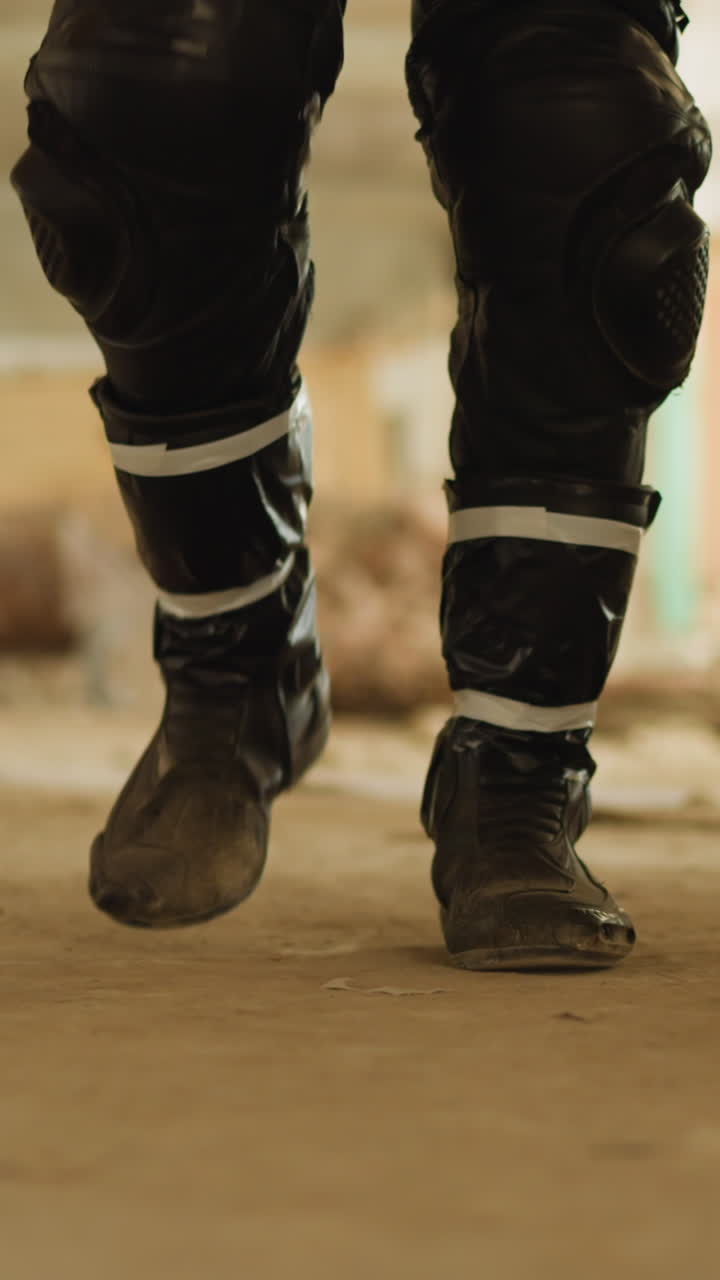 Man in black leather trousers and dusty boots walks along large empty hallway of old abandoned building extreme close view slow motion