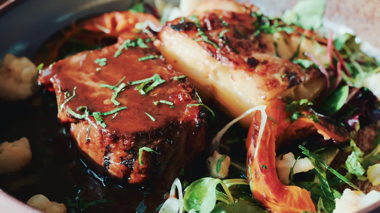 Close up of a gourmet meat dish with grilled vegetables, herbs, and rich sauce