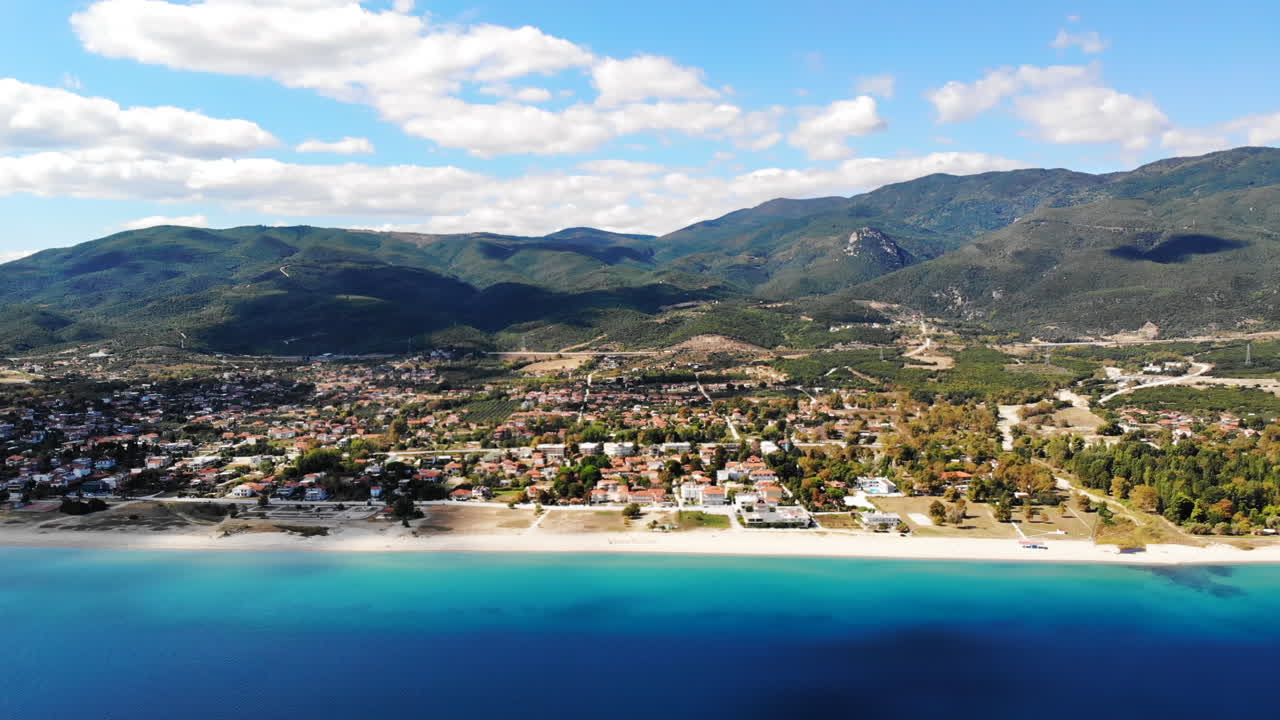 Asprovalta with multiple buildings and greenery, green hills on the background. Aegean sea coast. Long beach along the town. Sunny day. Greece