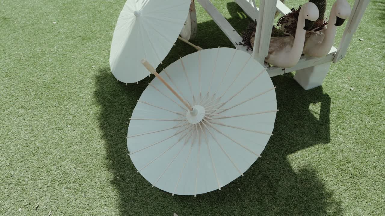 two white parasols resting on green lawn beside stylized flamingo decor