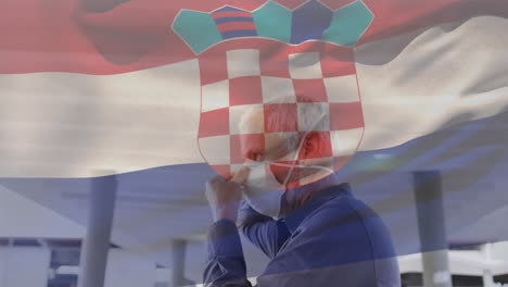 animation of flag of croatia waving over man wearing face mask during covid 19 pandemic