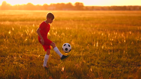 Ein-Junger-Junge-In-Einem-Roten-T-Shirt-Und-Turnschuhen-Jongliert-Bei-Sonnenuntergang-Mit-Einem-Fußball-Und-Trainiert-Und-Bereitet-Sich-Darauf-Vor,-Fußballspieler-Zu-Werden.-Der-Weg-Zum-Traum.-Harte-Arbeit