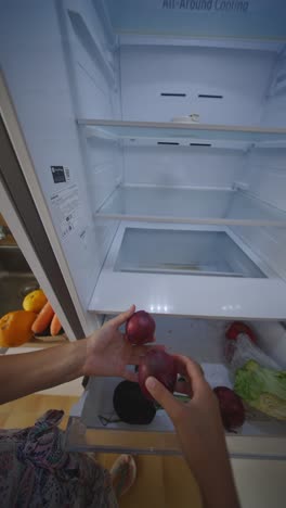 person putting onions in an empty refrigerator
