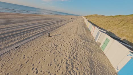 fpv drone shot of grassy dunes and an empty beach during a summer sunset