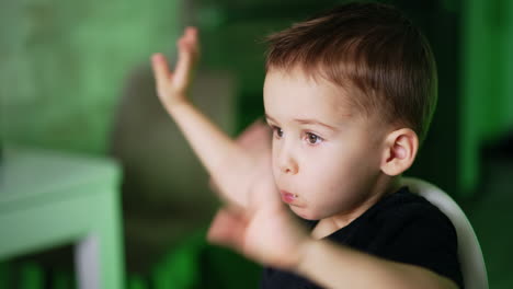 cute baby boy sitting in the chair and eating. caucasian kid chewing food and waving hands. close up. blurred backdrop.