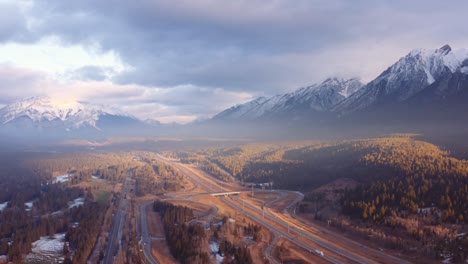 canmore alberta mountain range canadian rockies surrounding highway and overpass aerial sunrise drone shot pan away