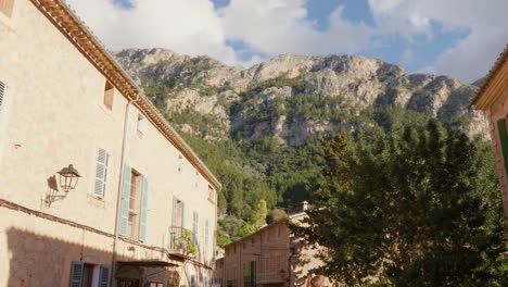 a street scene in deía, mallorca, spain, with mountains in the background and a blue sky scattered with clouds