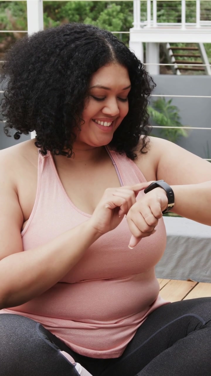 Vertical video: Ending routine woman in pink tank and leggings tapping black watch on deck for data