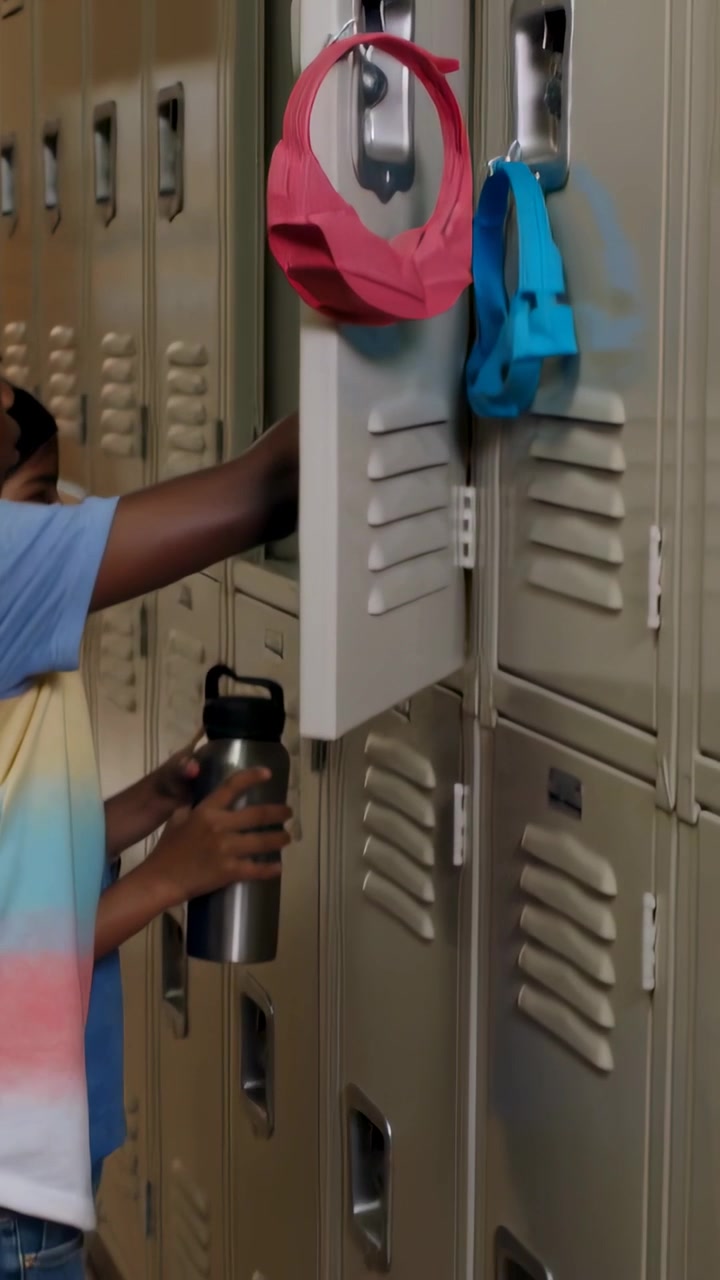 Vertical video: Walking child opening school locker, storing binder while holding bottle