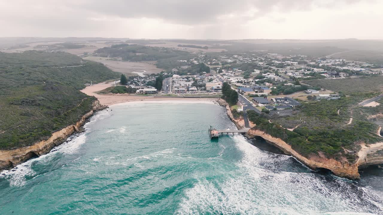 Drone footage captures the dramatic cliffs and ocean waves of Port Campbell, Australia, under overcast skies, highlighting natural beauty and coastal erosion