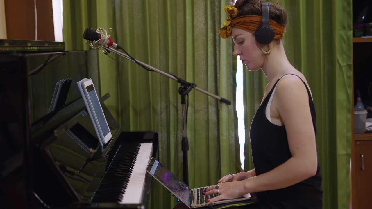 Woman recording music at a piano with headphones and laptop