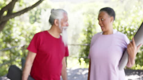 Happy-diverse-senior-male-and-female-friend-with-yoga-mat-talking-in-sunny-nature,-slow-motion