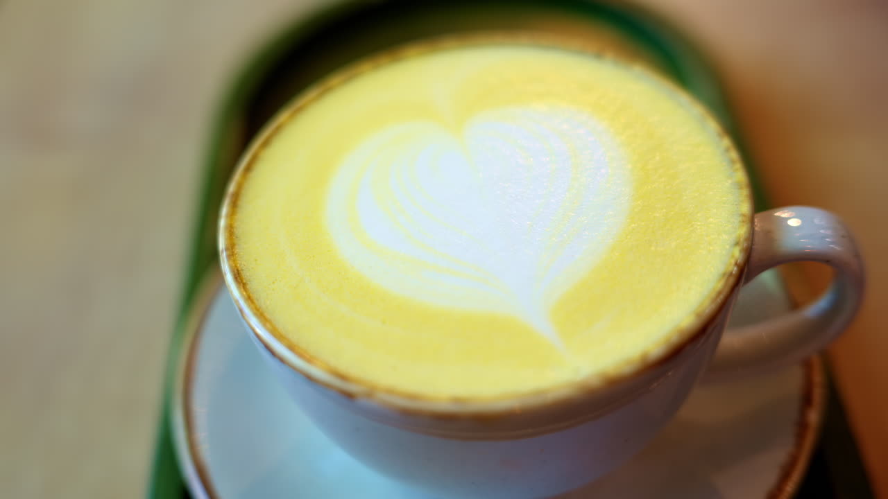 Close up of a cup of yellow turmeric latte with a heart design