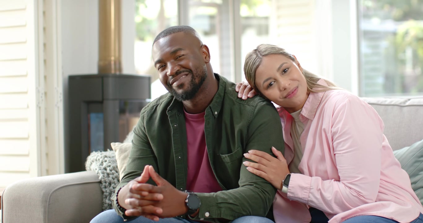 Couple sitting on sofa woman placing hand on man's shoulder, comforting him, smiling toward window