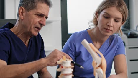 Two-caucasian-doctors-talking-and-showing-on-medical-models.