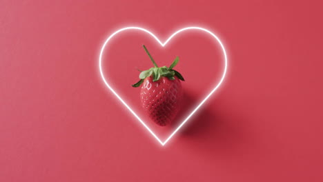 composition of neon heart and strawberry on pink background