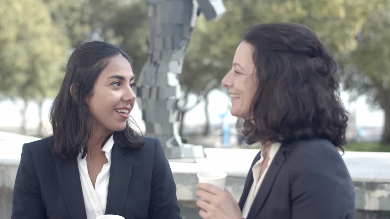 mujeres de negocios morenas bebiendo café al aire libre y hablando
