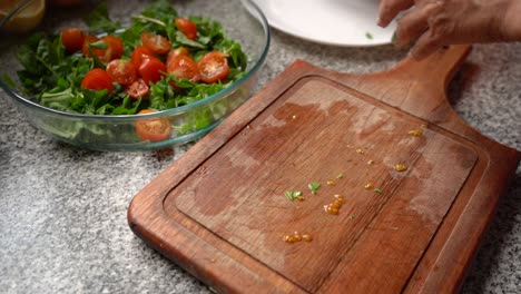 person placing the slice cherry tomatoes in a salad bowl with green leaves