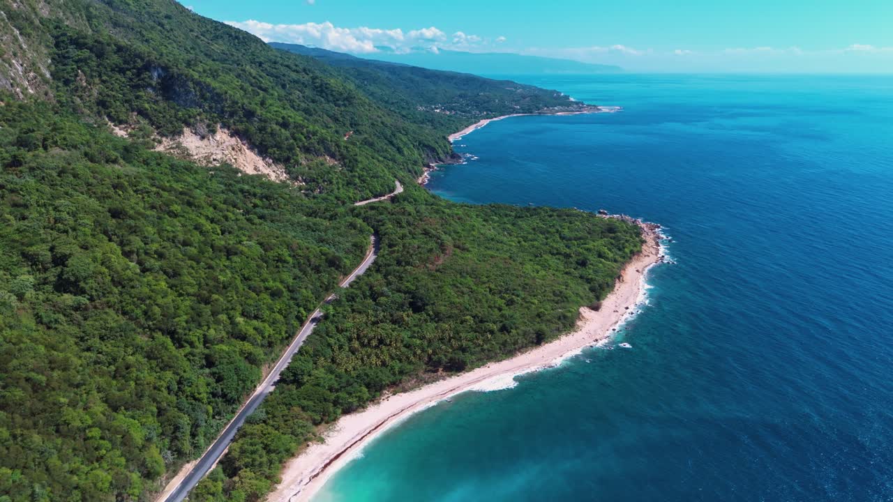 Aerial establishing shot of coastal road in green mountains of Barahona. Sandy soft beach and turquoise Caribbean Sea in summertime. Wide shot. Paradise on earth