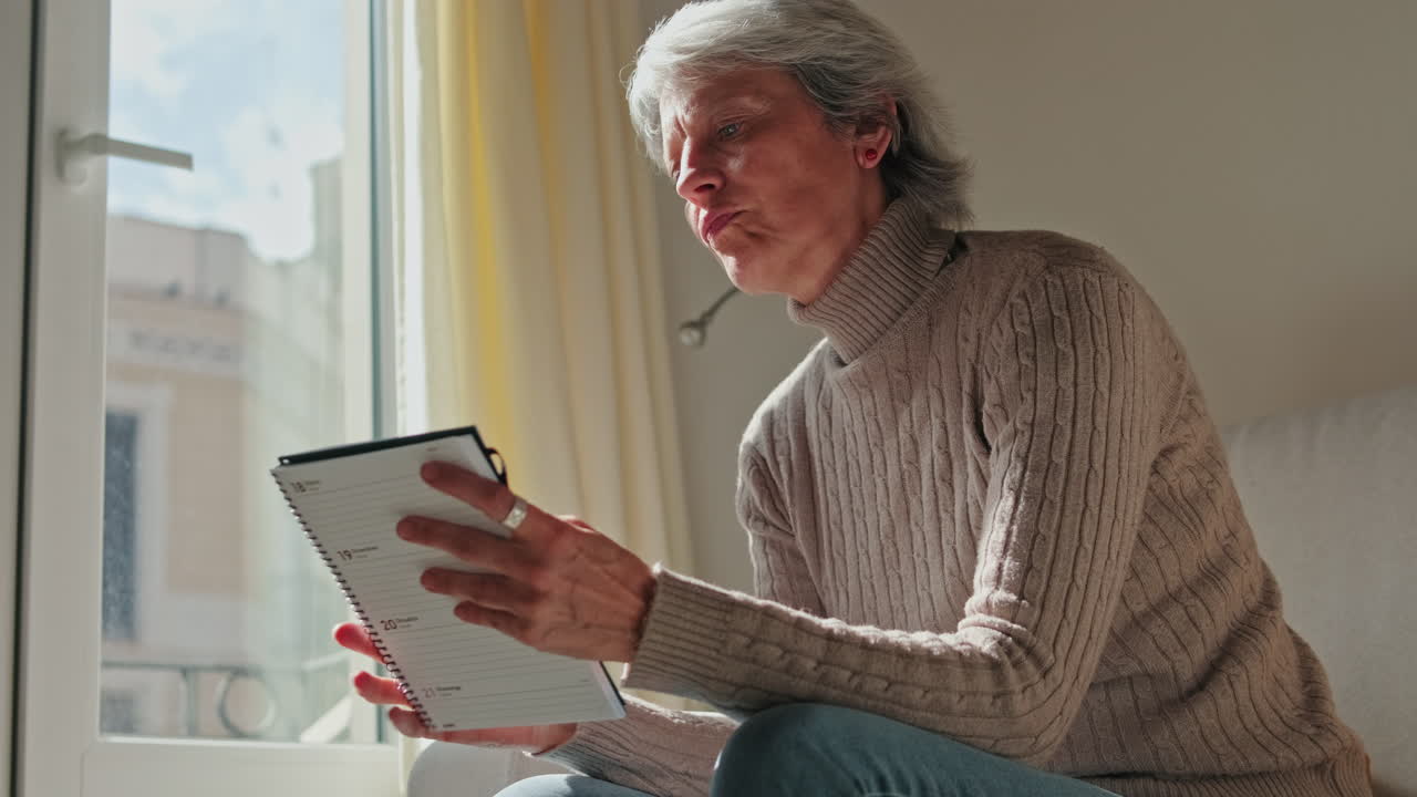 Mature Woman Thoughtfully Reading and Planning in Her Notebook at Home