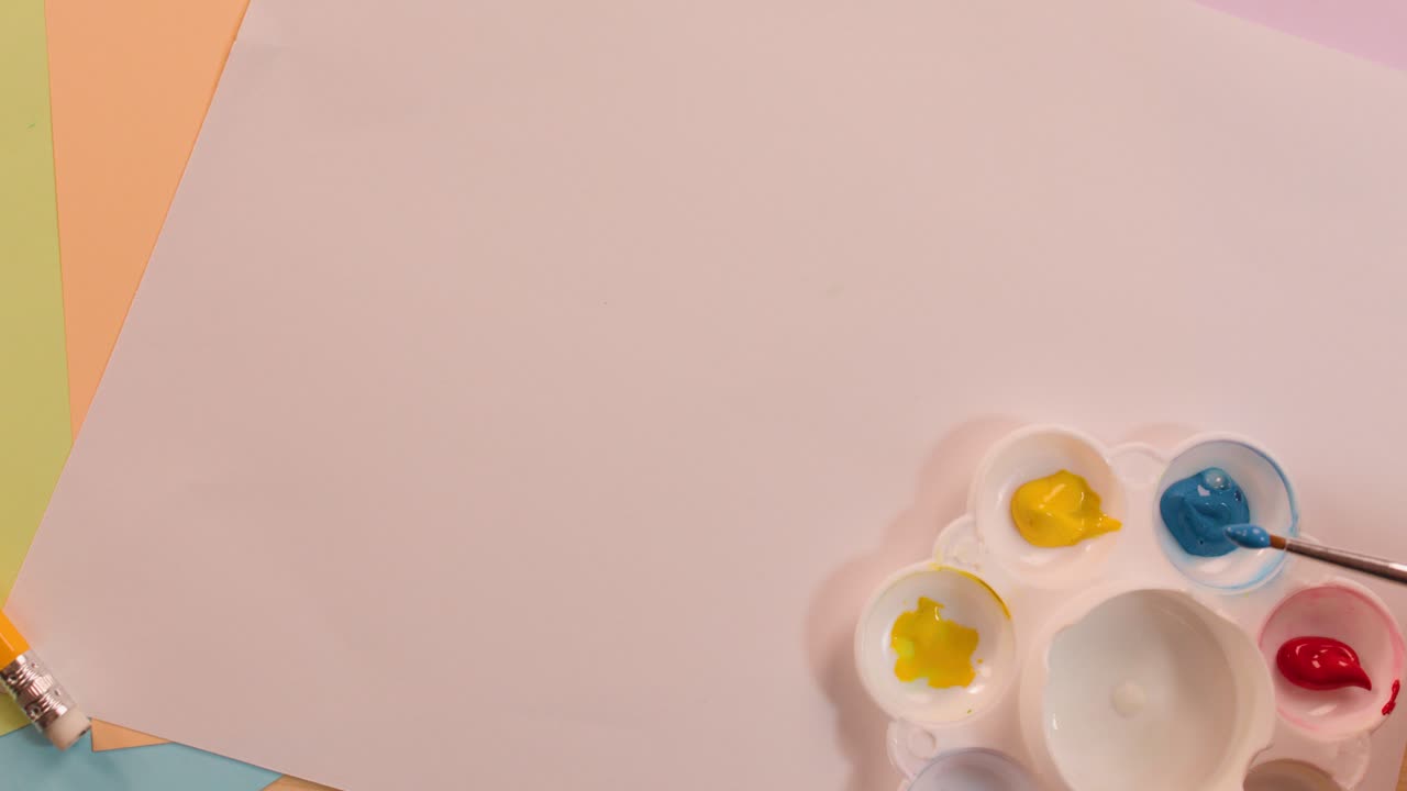 Hand mixes yellow and blue paint on palette, creating green, under soft lighting, overhead view