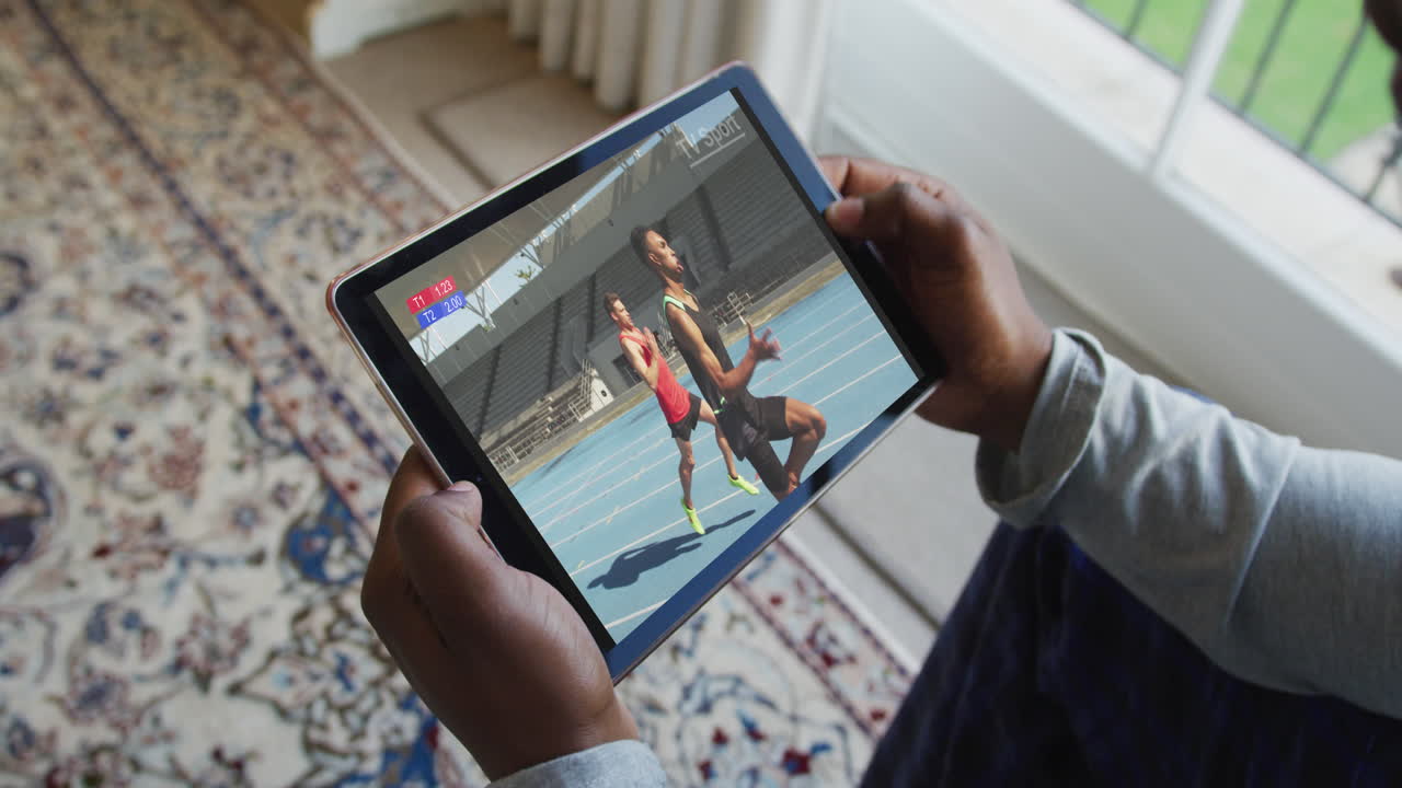 compuesto de un hombre sentado en casa viendo un evento de atletismo en una tableta