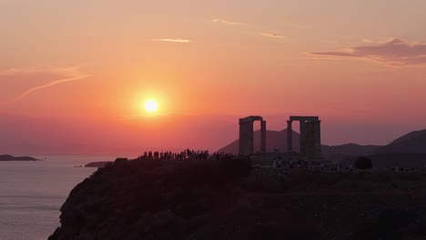 orbiting the temple of poseidon at sounio during sunset, revealing the ancient ruins, dramatic cliffs, and the glowing aegean sea horizon