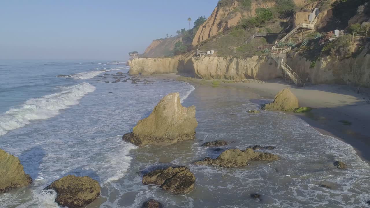 tomas aéreas de la playa el matador sobre olas y rocas en una brumosa mañana de verano en malibu, california