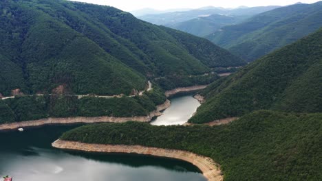 Flying-over-the-water-of-Vacha-dam-surrounded-by-mountain-and-green-forest