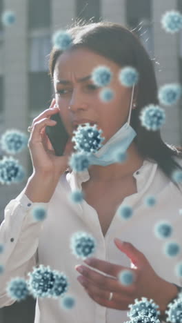 cellule di covid-19 galleggiano contro una donna con la maschera abbassata che parla su uno smartphone