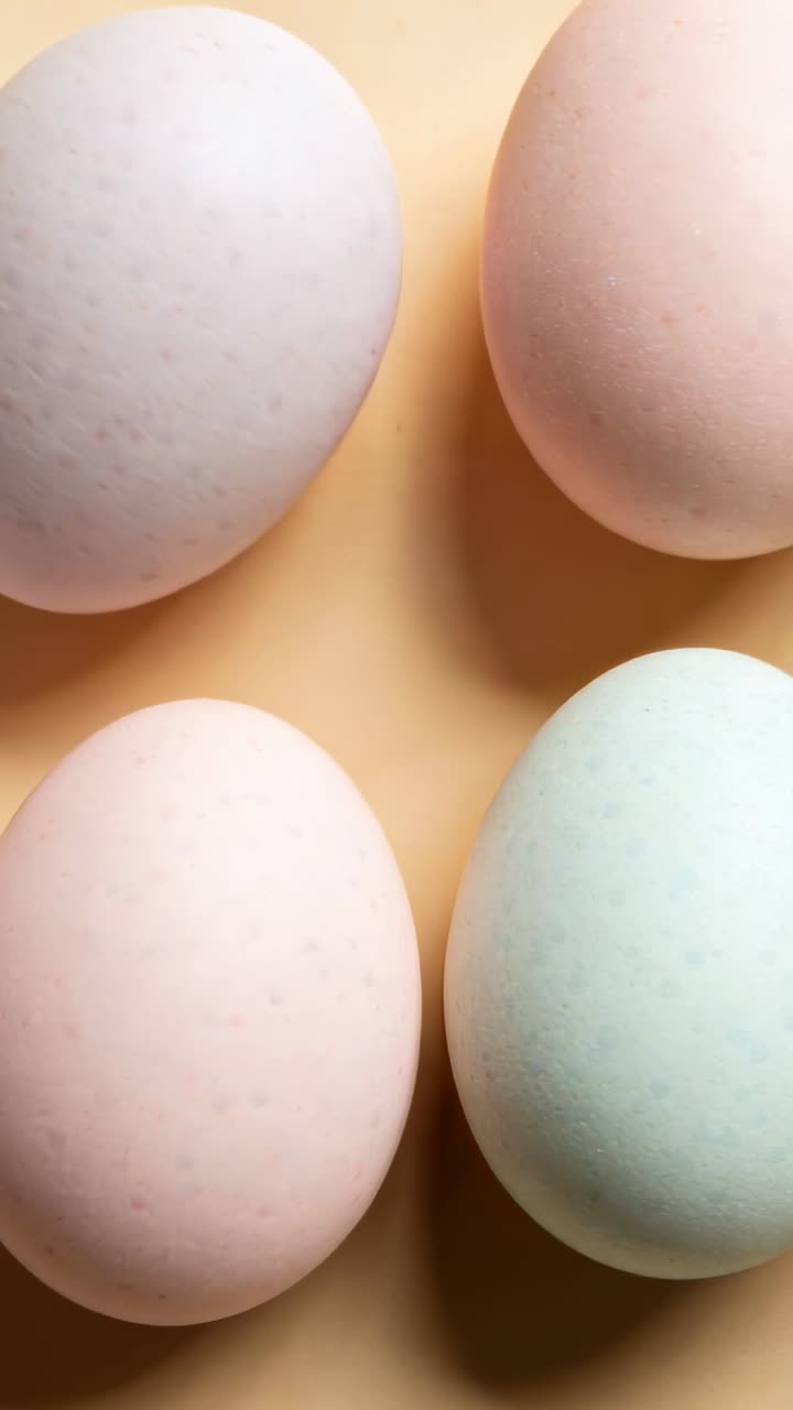 Showing four pastel eggs shifting subtly on peach tabletop with soft cast shadows