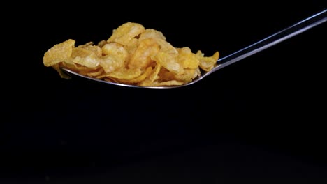 a spoon releases toasted corn cereal flakes, captured mid-air against a dark backdrop, highlighting texture and motion