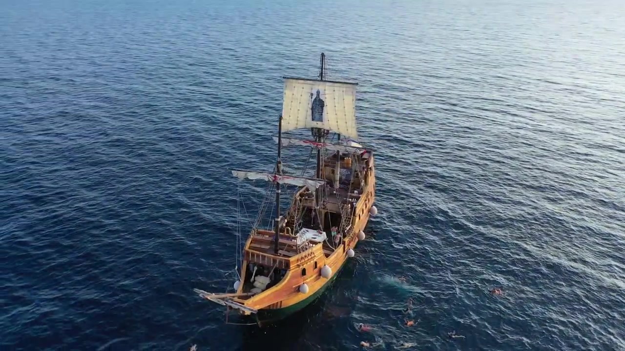 Splendide riprese con drone di una nave in legno in stile storico e barche a vela bianche ancorate in una cala turchese. Presenta spettacolari scogliere calcaree e lussureggianti pinete lungo la soleggiata costa adriatica