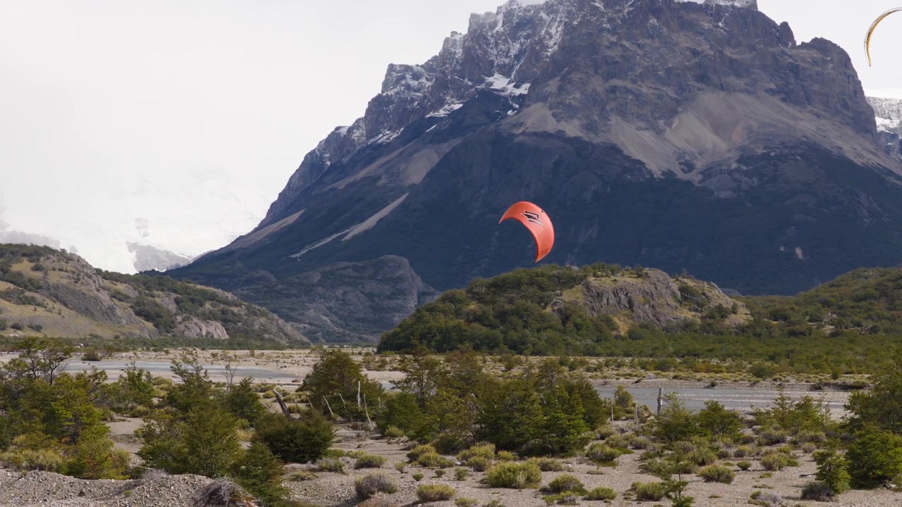 Paralotniarz leci nad Río de las Vueltas w pobliżu El Chaltén, Santa Cruz, Argentyna, przekraczając warkoczowatą równinę zalewową lodowca pod surowymi szczytami Masywu Fitz Roy, ujęcie śledzące z drona