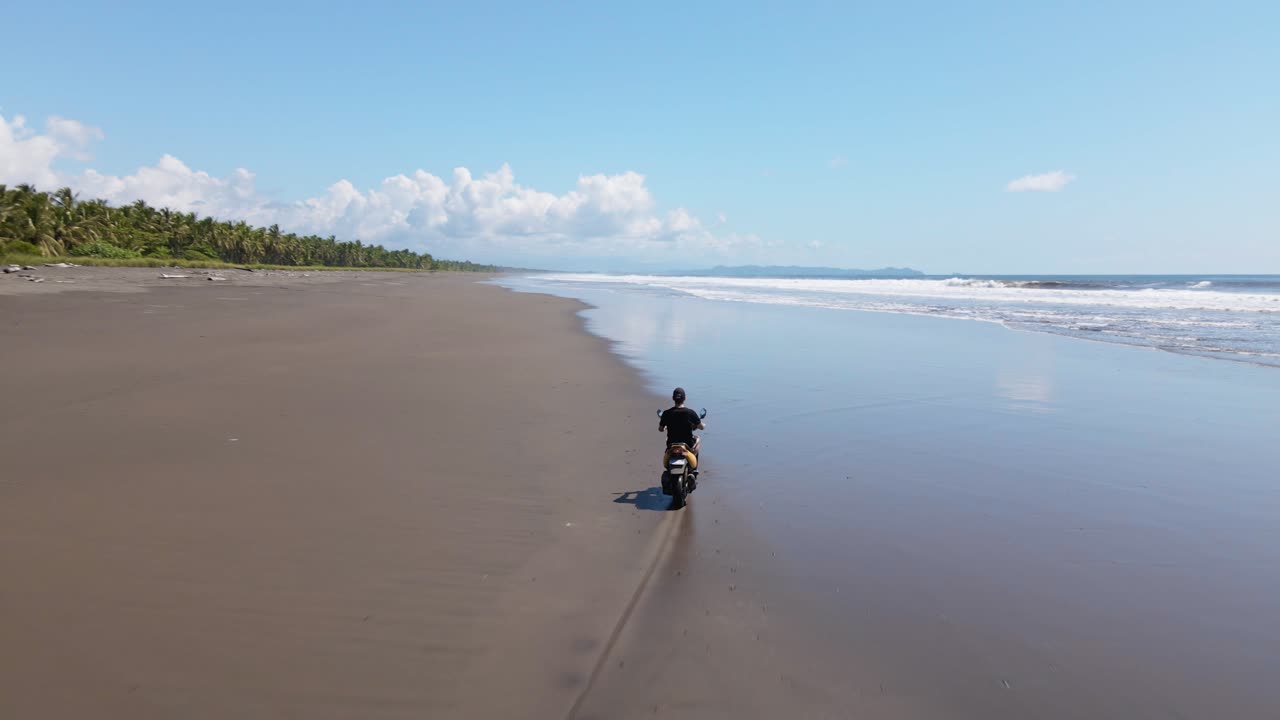 야자수와 따뜻한 태평양 사이의 그림 같은 해변을 따라 스쿠터를 타는 청년