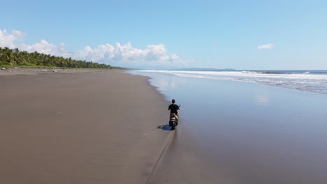 Young-man-riding-a-scooter-along-a-picturesque-beach-between-palm-trees-and-the-warm-pacific-ocean