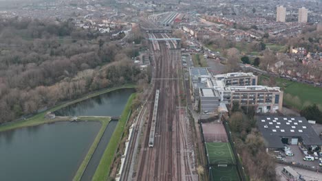 Overhead-follow-drone-shot-of-Thameslink-train-entering-small-London-suburb-station