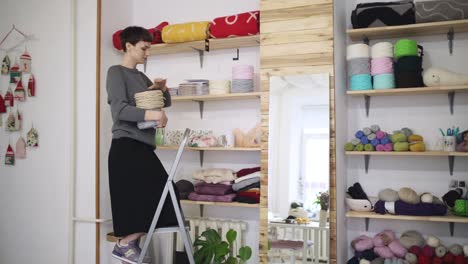 Creative-woman-shelving-thread-spool-on-stillage-in-textile-workshop