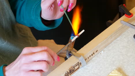 Craftsperson's-hands-holding-a-metal-rod-and-heating-glass-with-a-gas-torch-on-a-workbench