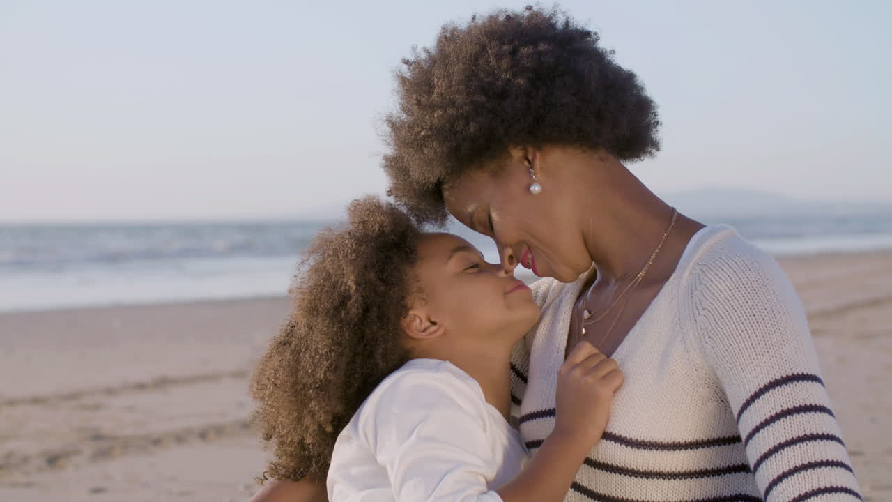 amorosa madre e hija abrazándose y tocándose la nariz en la playa