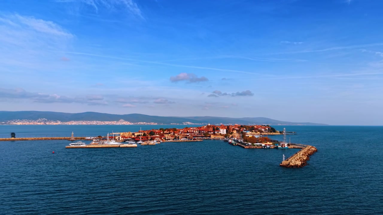 Marina ve uzaktaki dağlarla çevrili tarihi bir yarımada kasabasının geniş havadan görünümü. Yatların taş mendirekler boyunca sıralandığı dar bir deniz yarımadasında, arkasında dağların yükseldiği, kompakt bir tarihi kasaba yer alıyor.