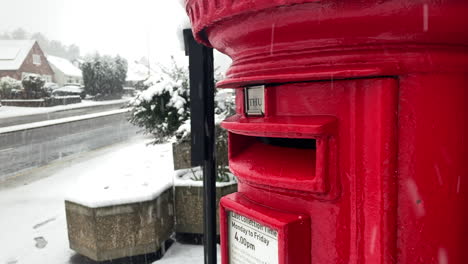 Close-up-of-a-classic-British-red-pillar-postbox-near-a-lampost-and-busy-road-in-the-snow-at-christmas