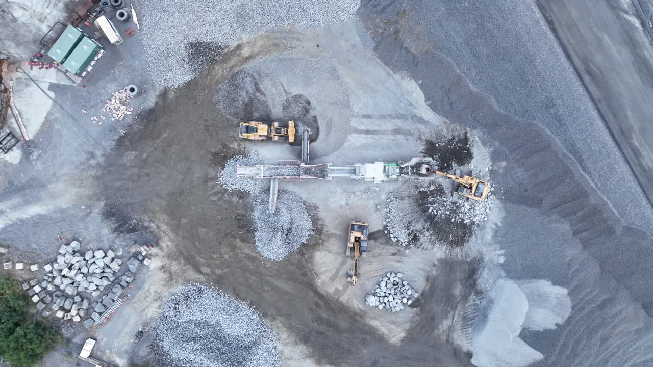 Drone shot of bob cat and mining excavator moving rocks, with conveyor belt sorting rocks with rubble into piles in quarry mine