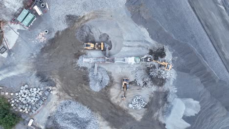 drone shot of bob cat and mining excavator moving rocks, with conveyor belt sorting rocks with rubble into piles in quarry mine