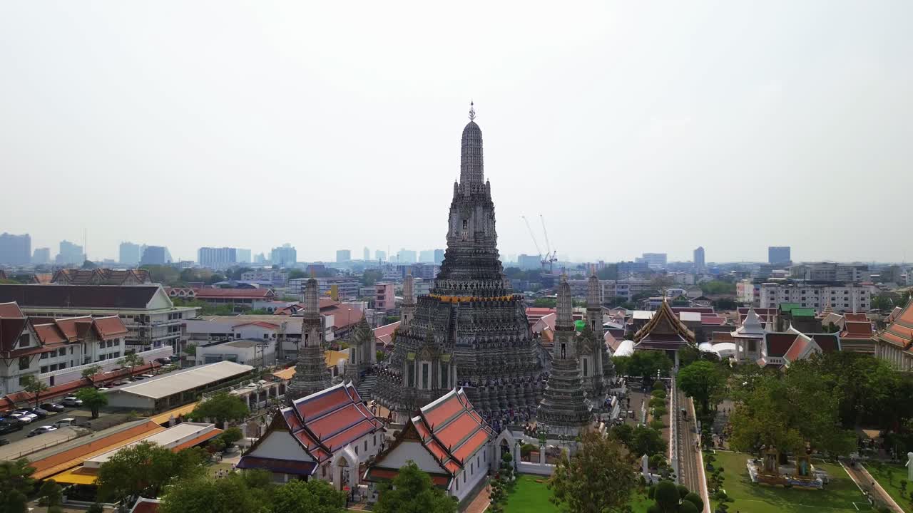 Aerial ascend of Wat Arun, Thailand iconic Temple of Dawn, towering spires along the Chao Phraya River with city backdrop