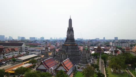 aerial ascend of wat arun, thailand iconic temple of dawn, towering spires along the chao phraya river with city backdrop