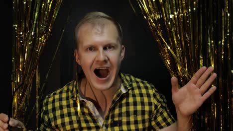 Portrait-of-caucasian-man-posing-on-black-background.-Gold-shining-foil-strips.-Party,-music,-disco