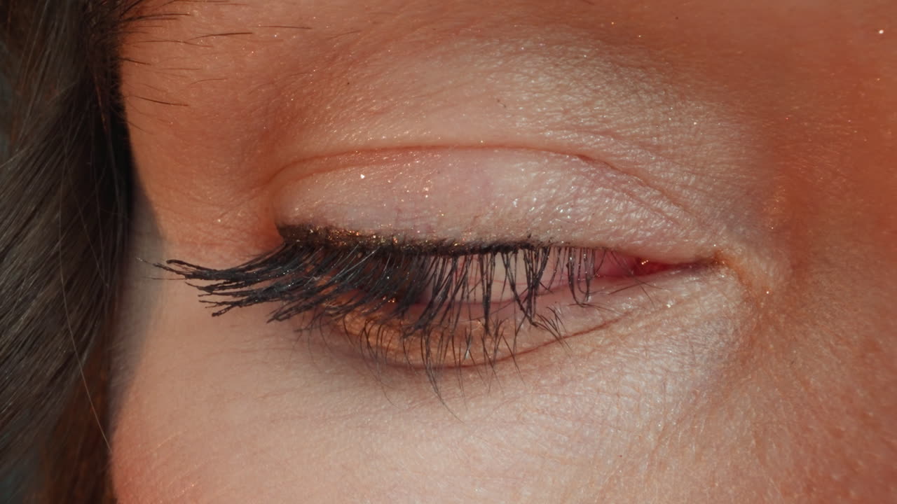 mujer joven abre los ojos con pestañas oscuras pintadas y brillo