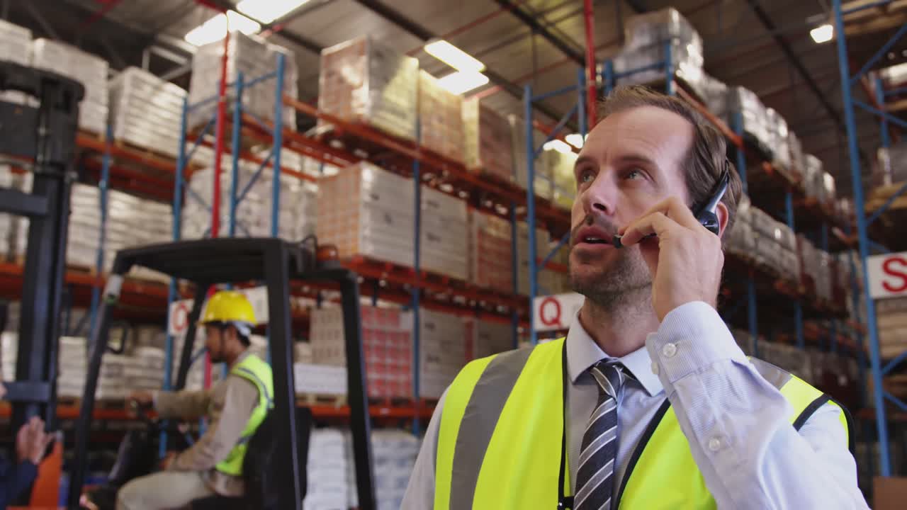 Male warehouse manager talking with headset in loading bay 4k